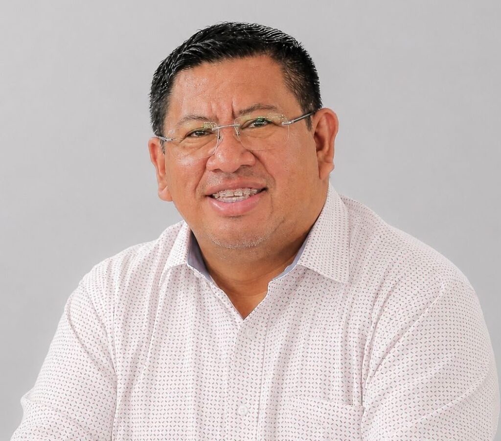 Luis Compá sonríe a la cámara; camisa blanca y fondo gris.