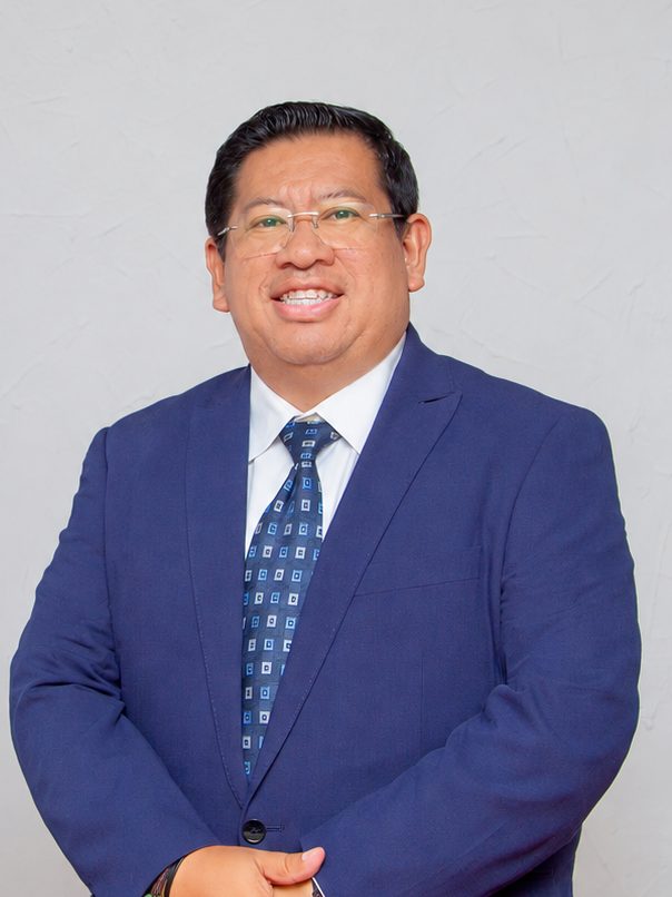 Luis Compá con traje azul y corbata, de pie, sonriendo.